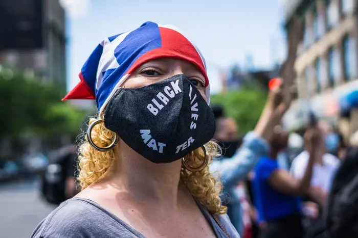 A woman wears a Puerto Rican flag bandana in her hair and a face mask that says "black lives matter"